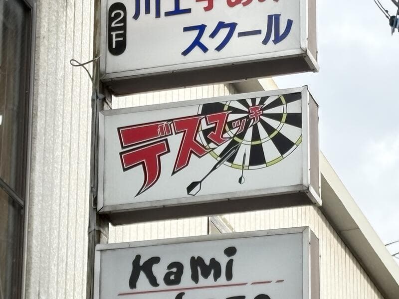 上田市中心部の縦並び看板に挟まれたダーツ風ロゴの「デスマッチ」看板