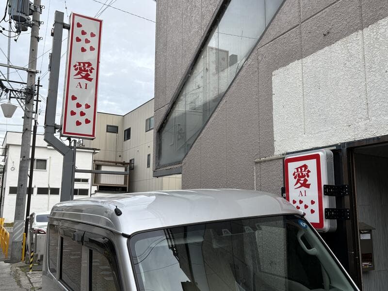 路地奥の白い袖看板に赤い「愛 AI」を掲げた看板