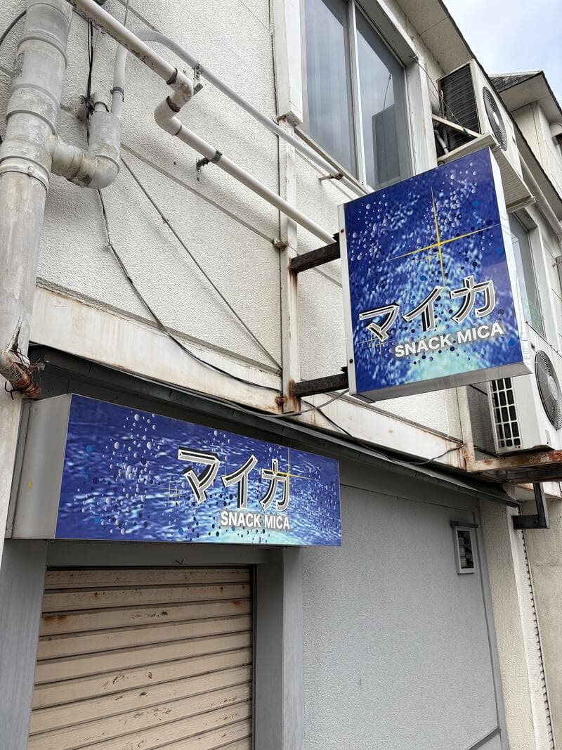 青い星空模様に金文字を重ねた「マイカ SNACK MICA」看板