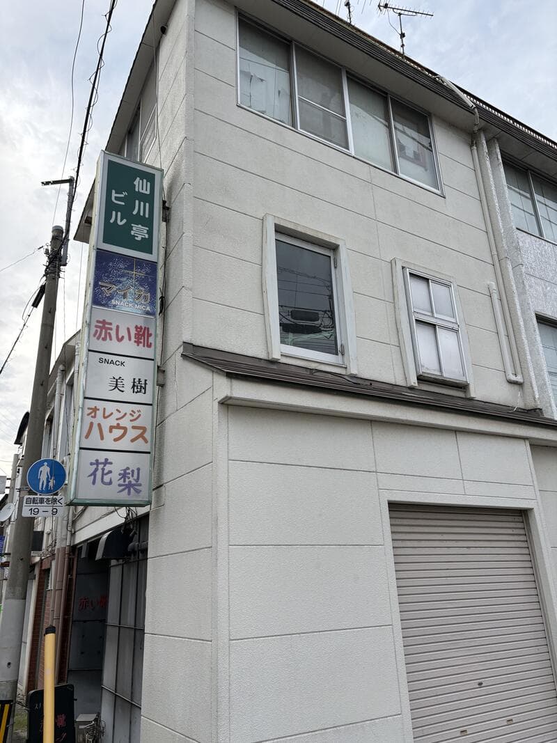 外壁の縦看板に並ぶ「赤い靴」「オレンジハウス」「花梨」などの店名群