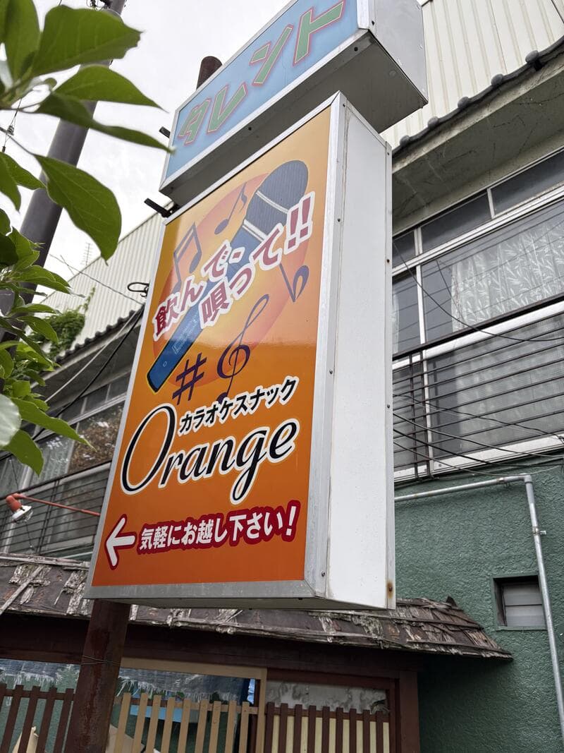 オレンジ色の縦看板に音符を散らした「カラオケスナック Orange」