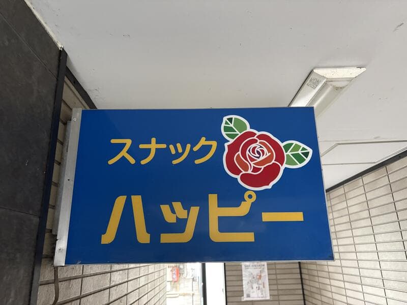 青地に黄色文字とバラを添えた「スナック ハッピー」看板