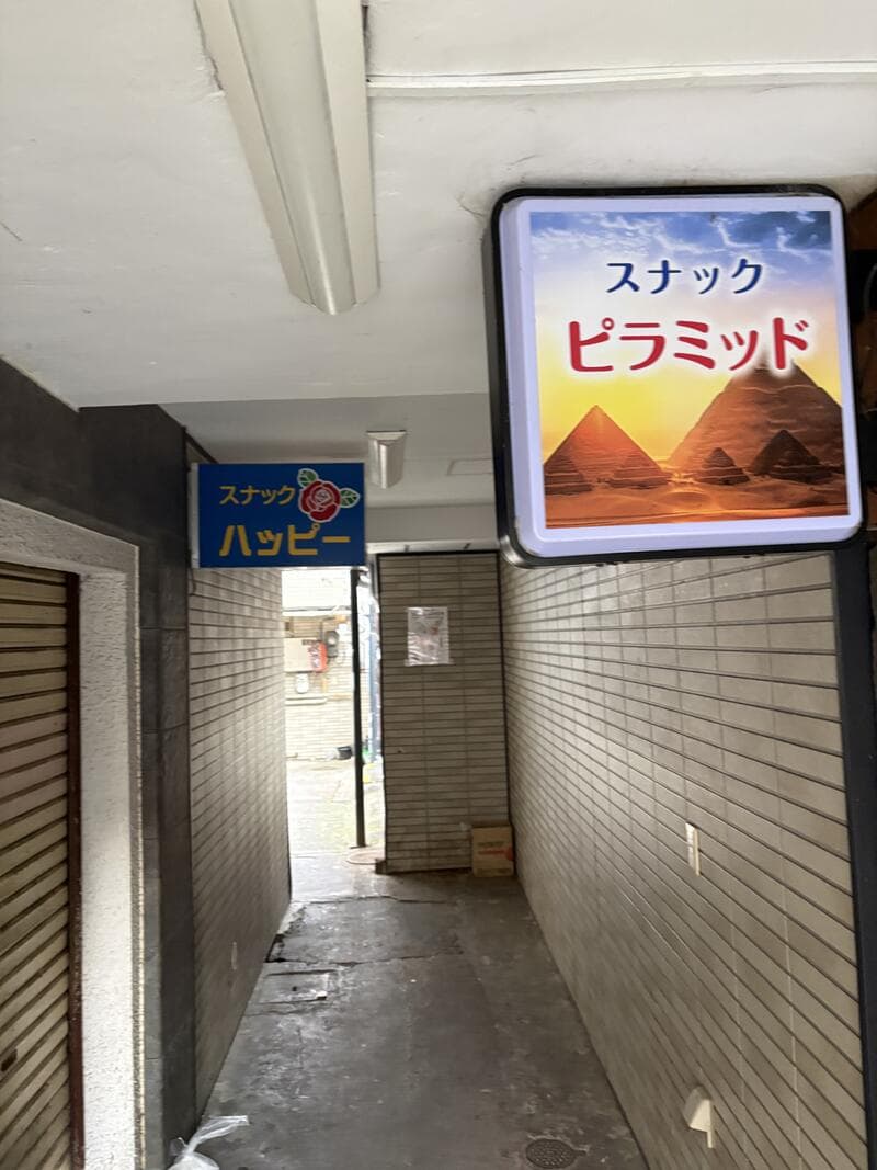 通路の奥に「ハッピー」と「ピラミッド」が並んで見える看板風景