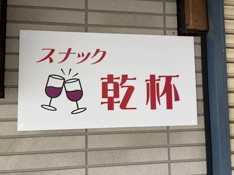 グラスのイラストを添えた白い「スナック 乾杯」看板