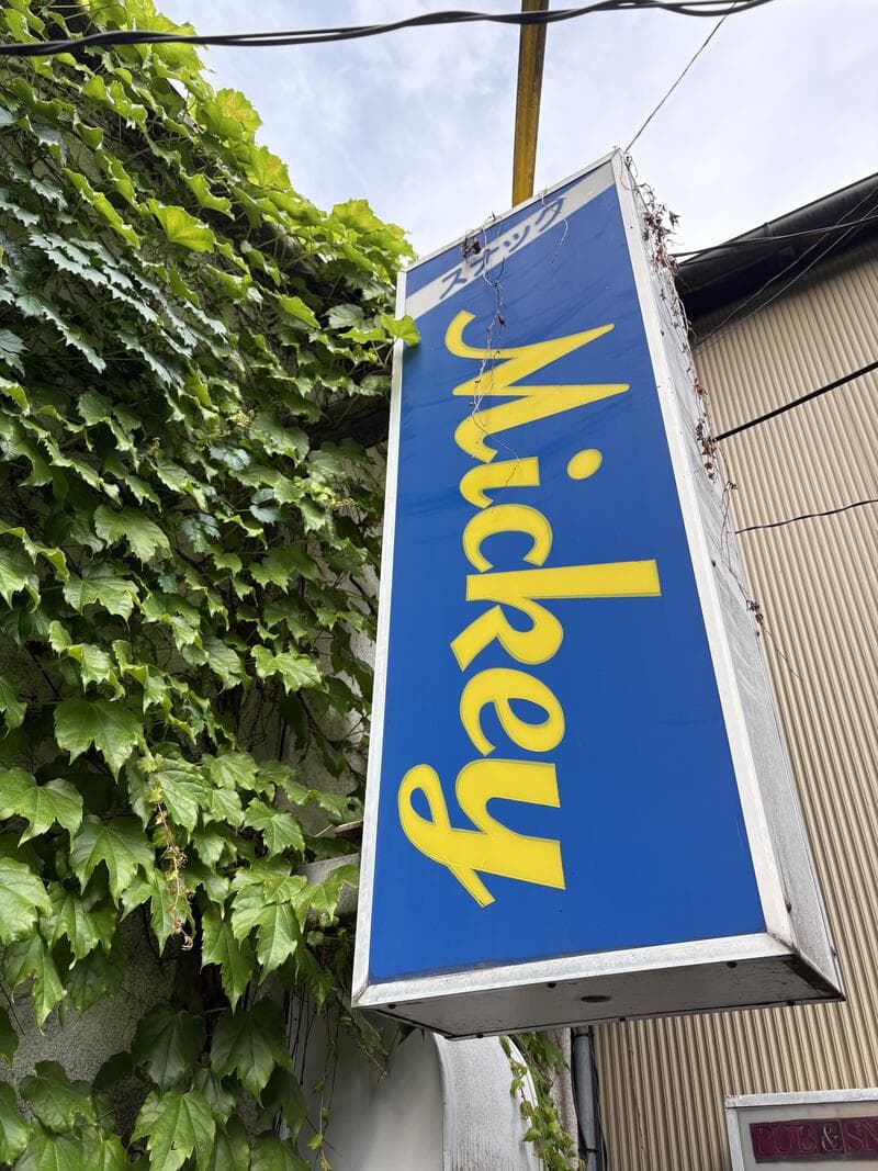 蔦の壁から突き出す青い「Mickey」の袖看板