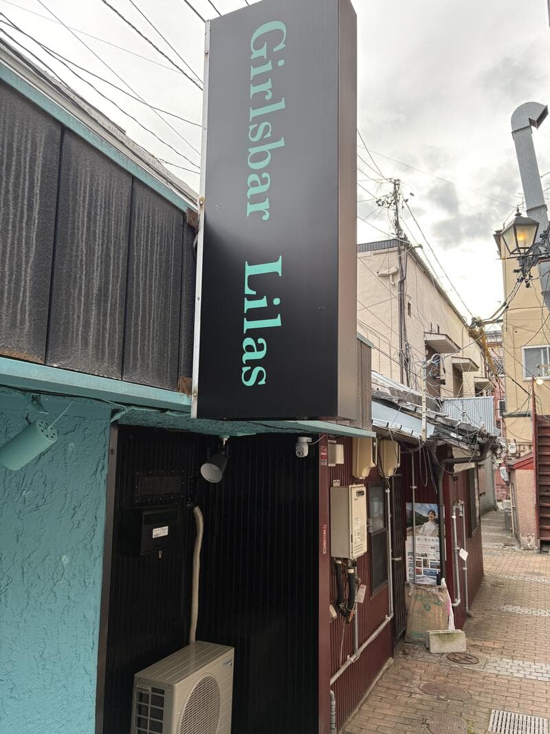 黒い縦看板に水色文字を配した「Girlsbar Lilas」