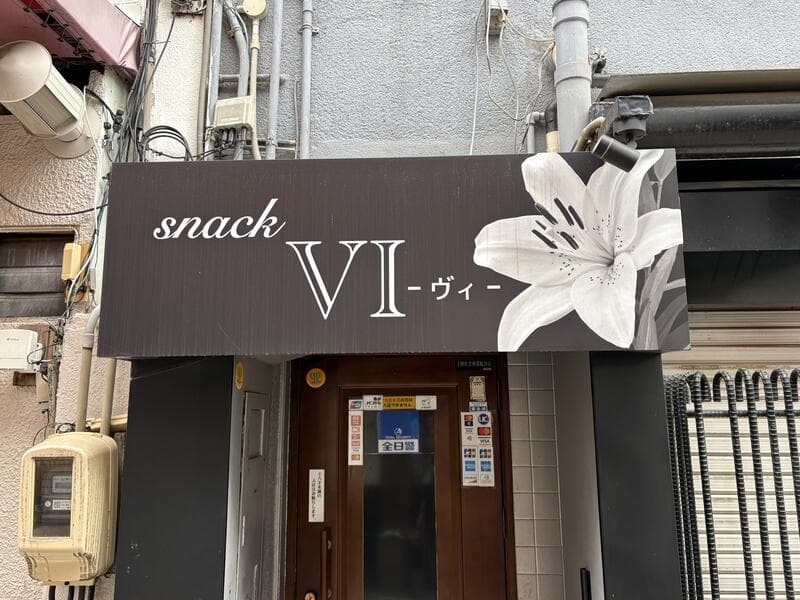 大きな白いユリを添えた黒い「snack VI」入口看板