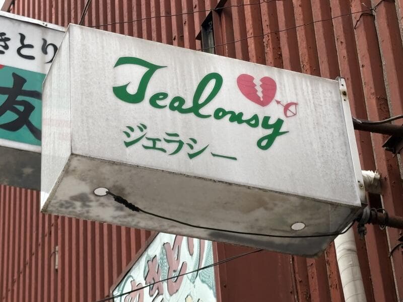緑の筆記体と花を添えた白い「Jealousy」袖看板