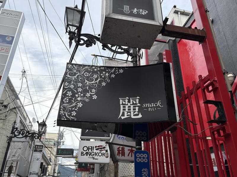 黒い袖看板に白い花模様を添えた「麗 snack」看板