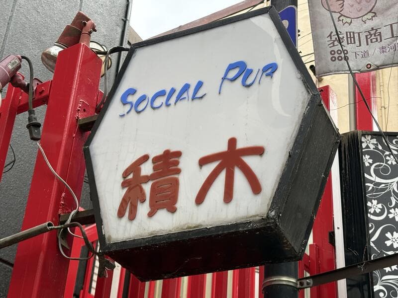 白い袖看板に青字と赤字で書かれた「Social Pub 積木」
