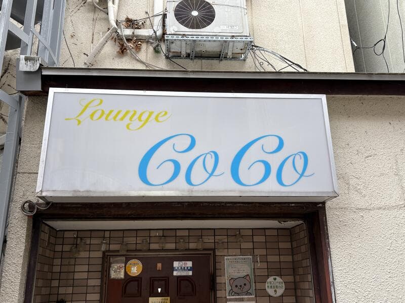 白地に水色の筆記体を置いた「Lounge CoCo」看板