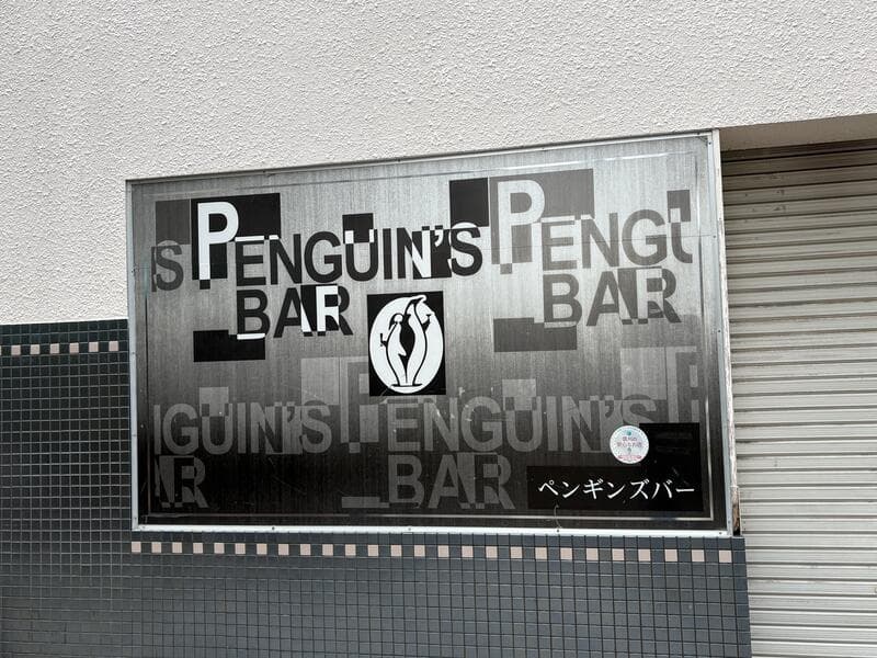 モノクロ調の面板に反復文字を重ねた「PENGUIN’S BAR」看板