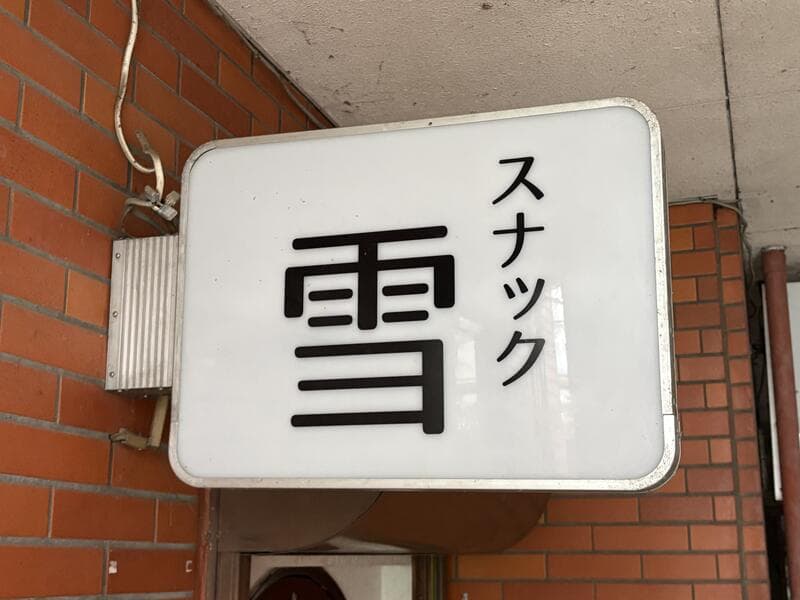 白い箱看板に太い黒文字を置いた「スナック 雪」