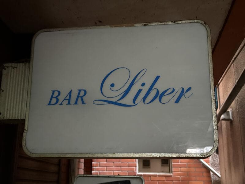 白い面板に青い筆記体を置いた「BAR Liber」看板