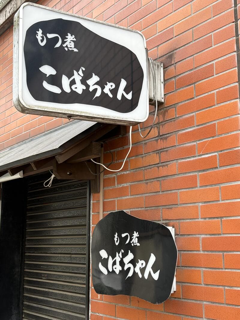 黒い筆文字の「もつ煮 こばちゃん」看板