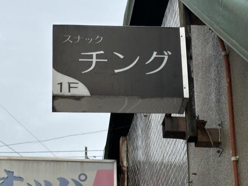 黒い面板に白文字を置いた「スナック チング」看板