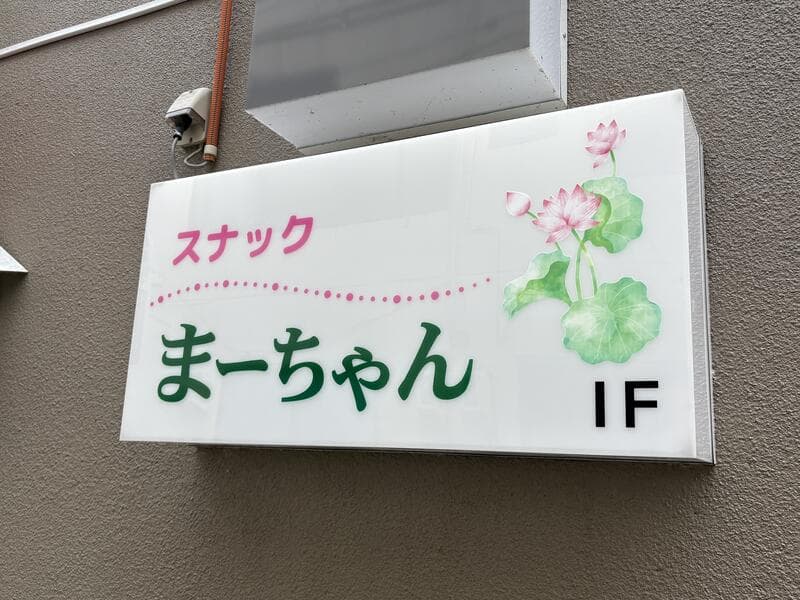 花のイラストを添えた白い「スナック まーちゃん」看板
