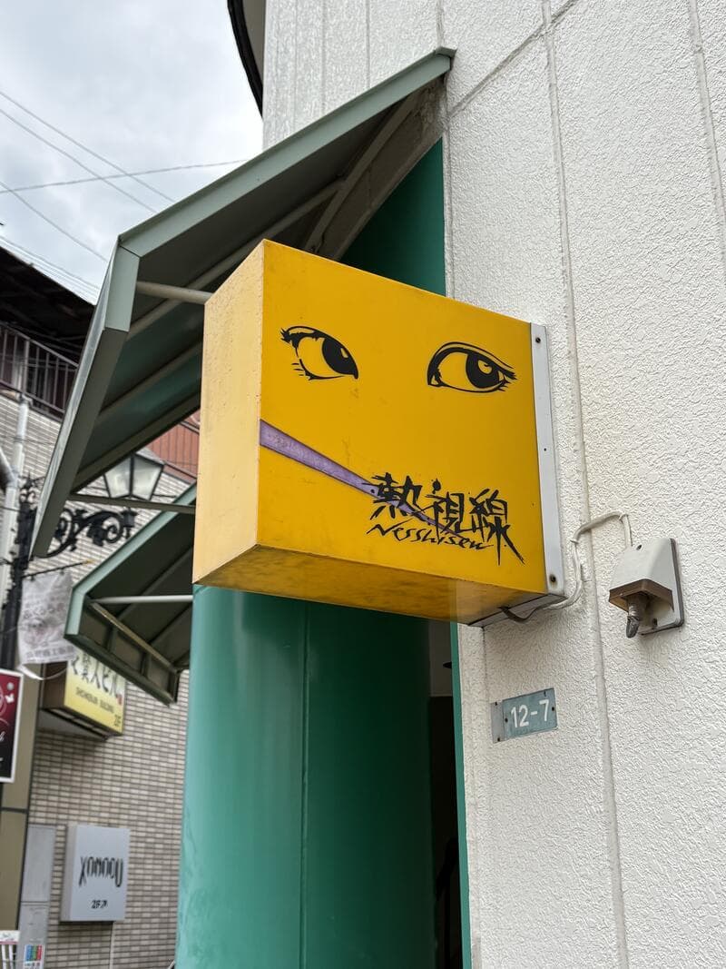 白い外壁から突き出す黄色い「熱視線」袖看板