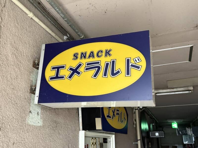 黄色楕円と青地で作られた「SNACK エメラルド」看板