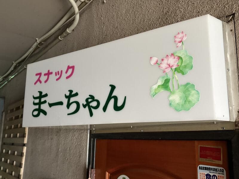 花のイラストを添えた白い「スナック まーちゃん」入口看板