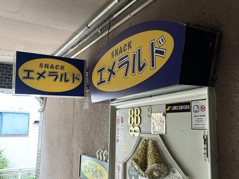入口に二つ並ぶ青と黄色の「SNACK エメラルド」看板