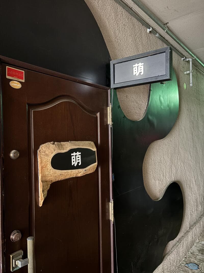 黒い曲面壁と木扉で構成された「萌」の入口
