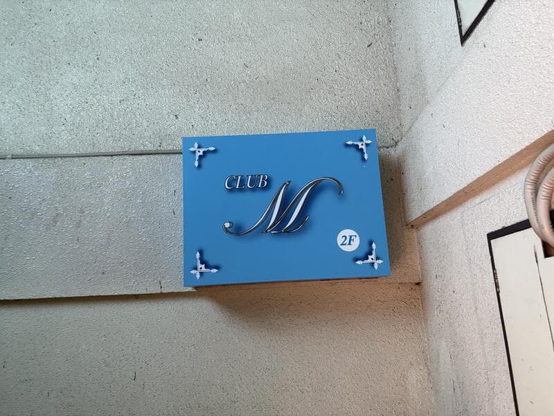 水色の面板に筆記体ロゴを置いた「CLUB M」看板