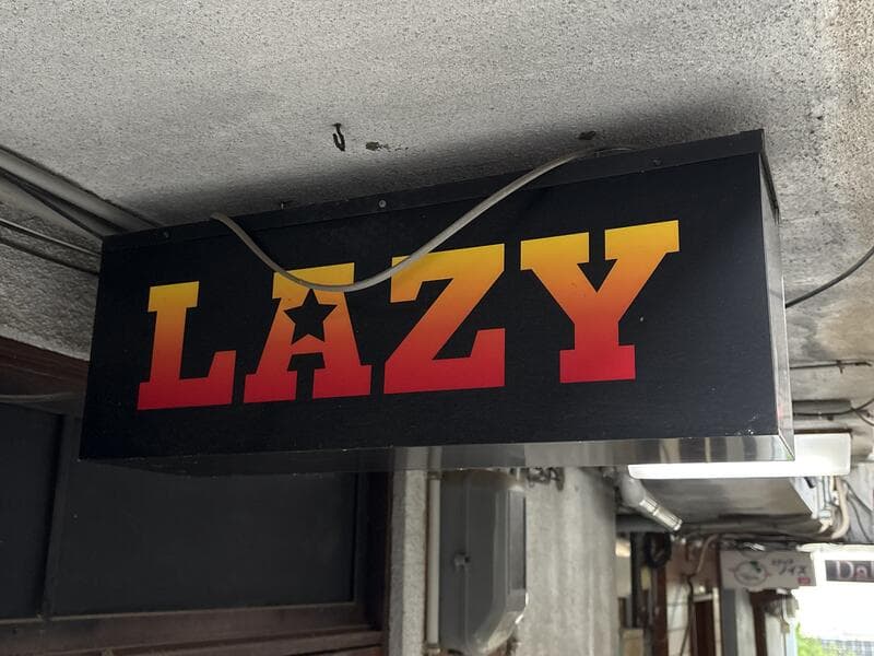 黒地に赤黄文字の「LAZY」看板