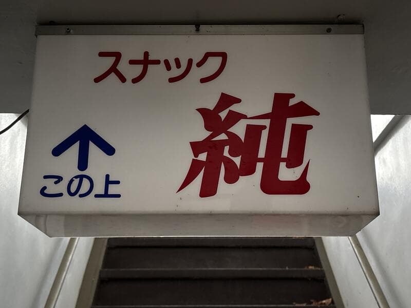 「この上」案内付きの白地「スナック 純」看板
