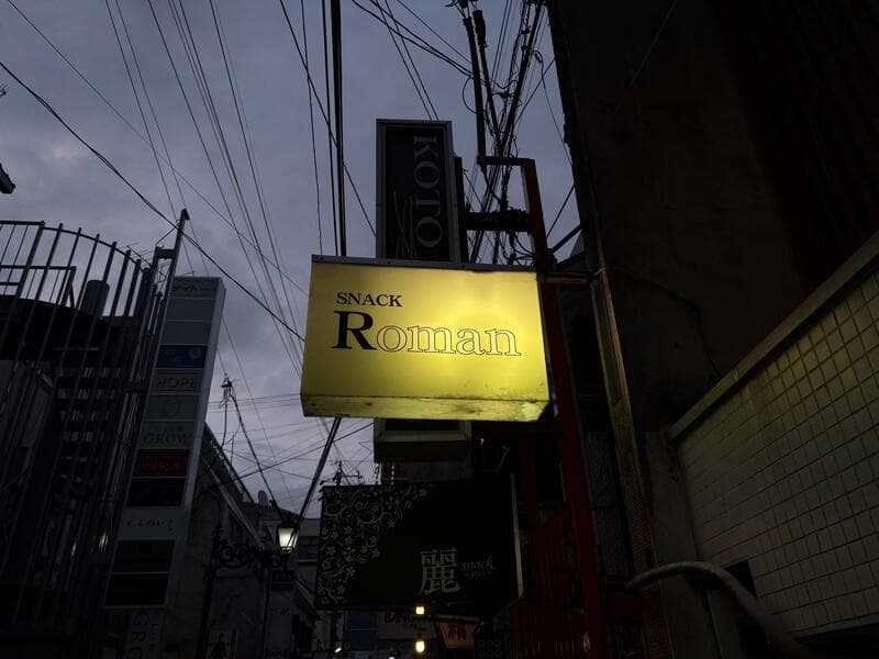 灯る黄色い「SNACK Roman」看板の路地風景