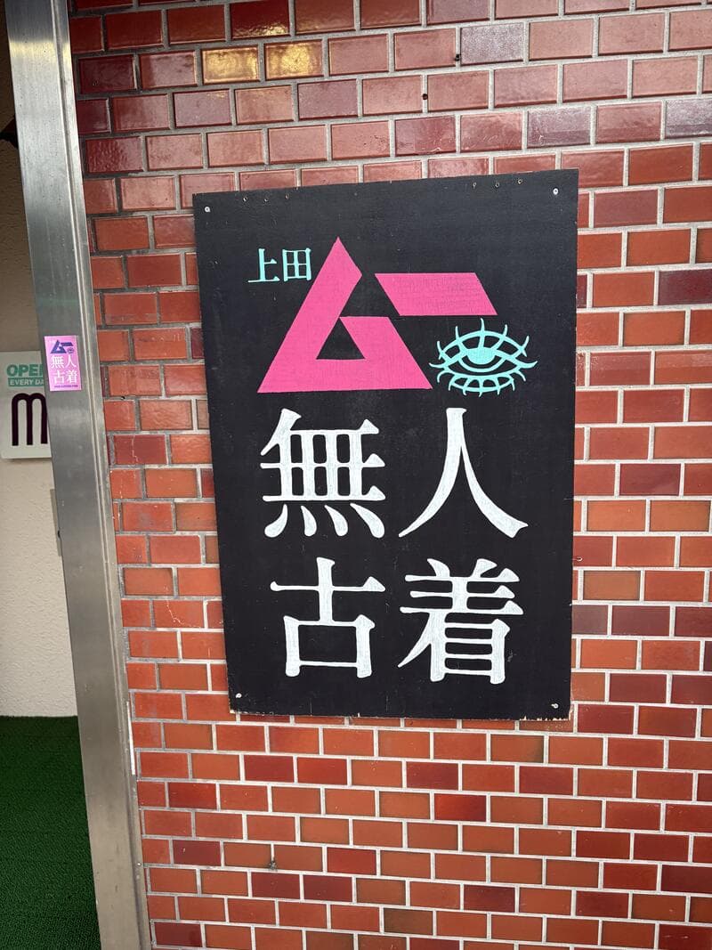 上田の煉瓦壁に掛かった『無人古着』の黒地ロゴ看板